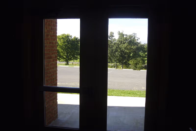Dark interior doorway opens to a bright exterior with a parking lot and trees beyond.