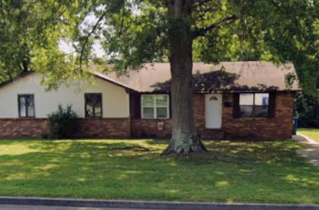 Front view of a single-story brick building with a green lawn and a large tree.
