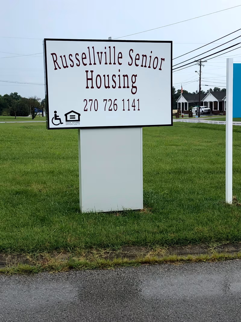 A large Russellville Senior Housing sign on a grassy lot with distant buildings visible.