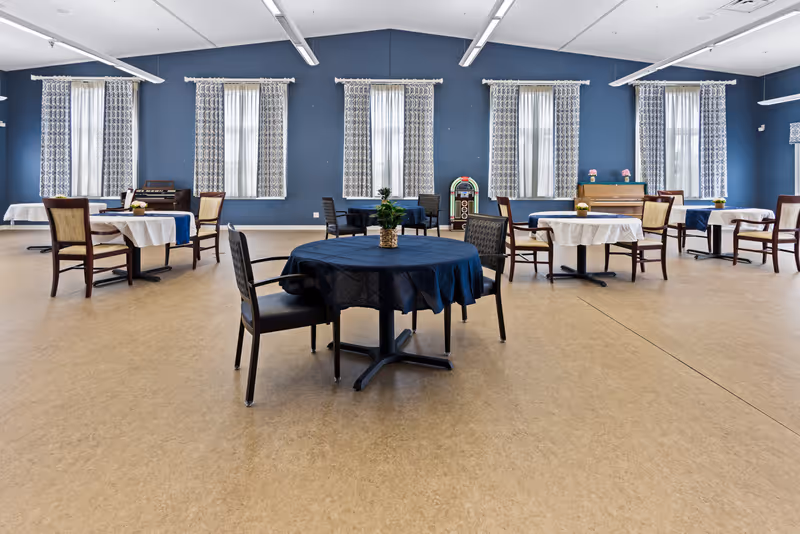 A spacious dining hall with round and rectangular tables, chairs, and blue walls.