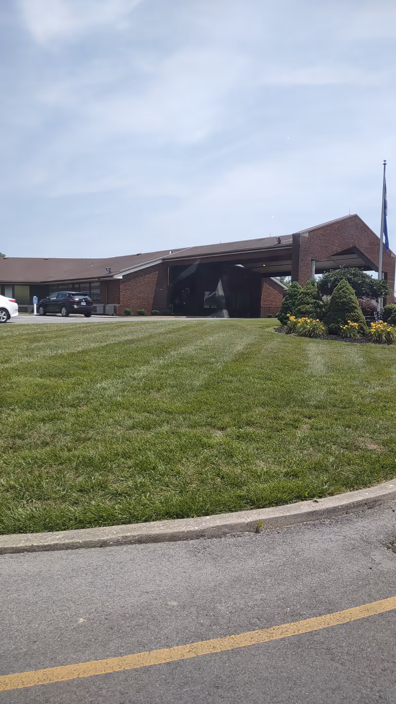 Exterior view of a brick senior living facility with a manicured lawn and driveway.