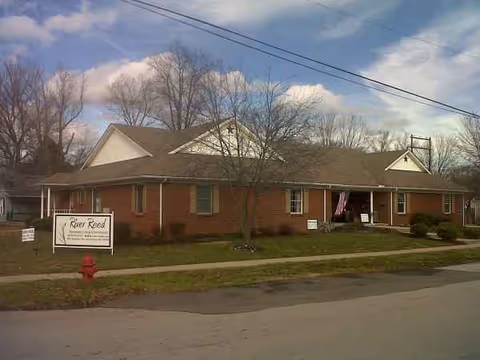 A single-story brick assisted living facility with a sign out front and trees nearby.
