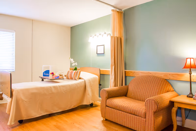 A patient room with bed, sofa, nightstand, lamp, and green accent wall.