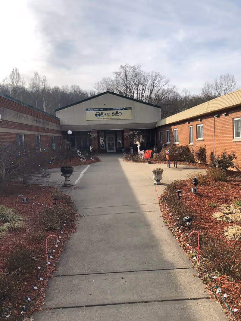 Wide walkway to River Valley Nursing Home entrance; brick building with seasonal landscaping.