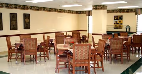 Open dining room with several wooden tables and upholstered chairs in a well-lit communal space.