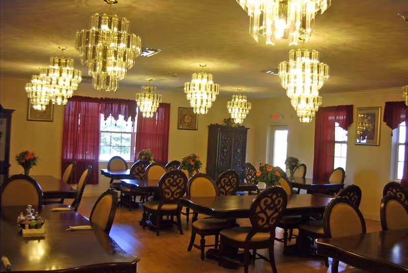 Interior dining room with crystal chandeliers, dark wooden tables, and floral centerpieces.