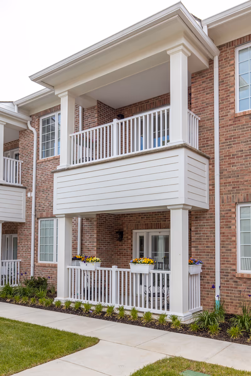 Exterior view of a brick senior living building with white balconies and planters.