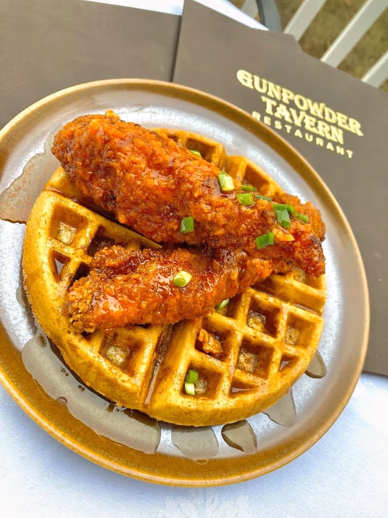 Crispy fried chicken tenders with sauce and chopped green onions served on a waffle on a plate next to a menu.