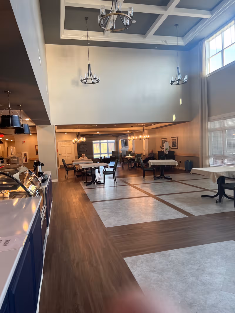 Bright, spacious dining area with chandeliers and resident tables in a senior living facility.