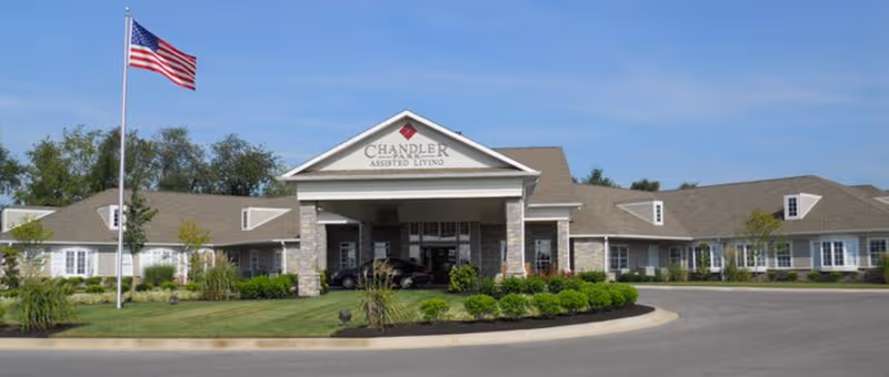 Front entrance of a single-story senior living facility with a circular driveway and flag.