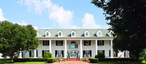 Front view of white, columned rehab center with manicured lawn.
