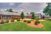 Single-story brick health and rehabilitation center building with a landscaped lawn, mulch beds, and shrubs under a cloudy sky.