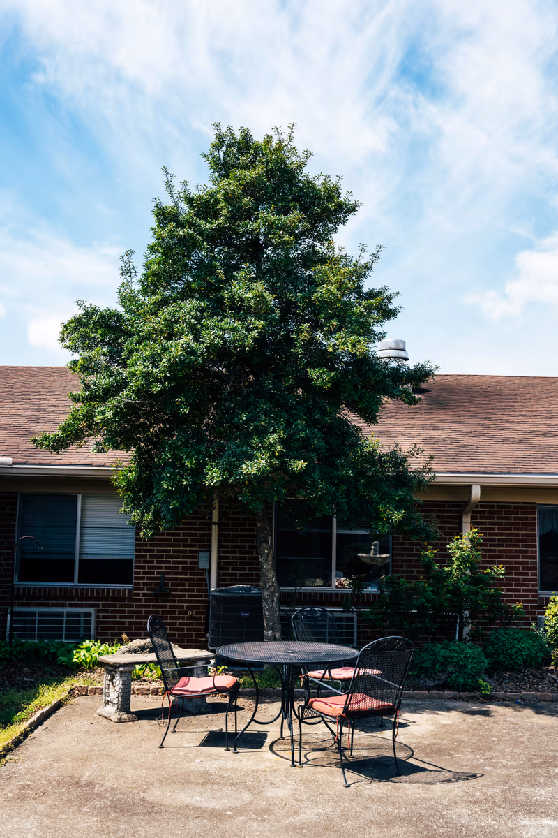 Outdoor courtyard with a round metal table and chairs under a tree in a brick building.