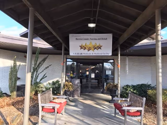 Covered entry to Barren County Nursing and Rehab with benches and a sign.