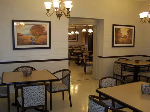 Interior dining room with tables, chairs, and framed landscape paintings.