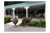 Covered outdoor pavilion with picnic tables, a decorative urn planter, and surrounding landscaping in front of a building.