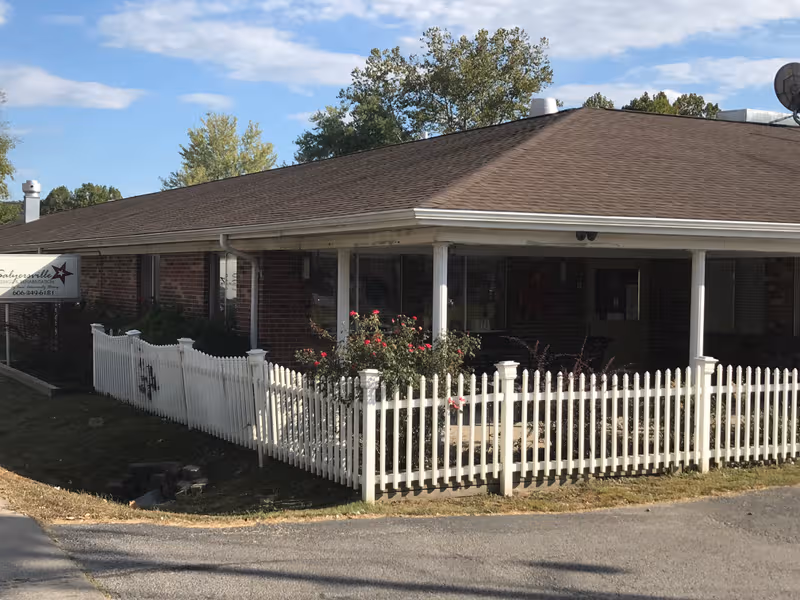 Single-story brick facility with a white picket fence and front entrance, Salyersville Nursing & Rehab.