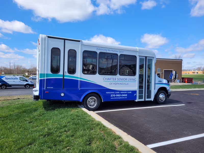 Blue Charter Senior Living bus labeled Hopkinsville parked in a lot with building behind.