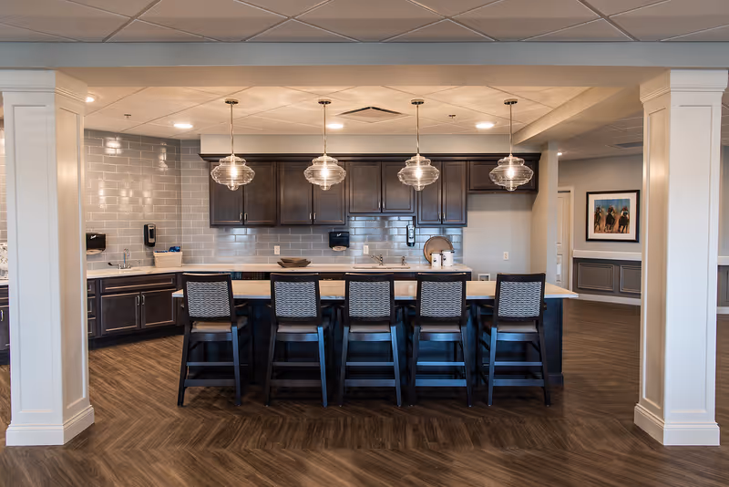 Modern communal dining area with a long kitchen island and pendant lights.