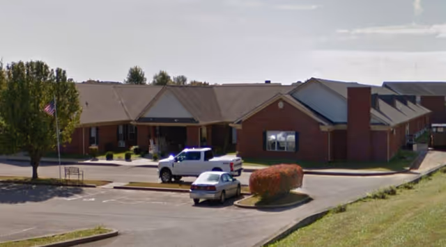 Exterior view of Bluegrass Assisted Living building with parking lot and landscaped grounds.