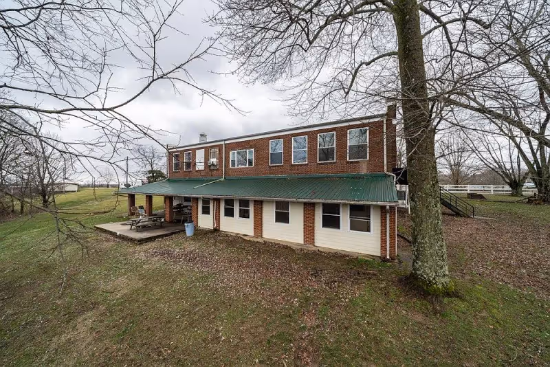 Two-story brick building with a green metal roof and covered patio with a picnic table, set on a grassy lot with leafless trees.