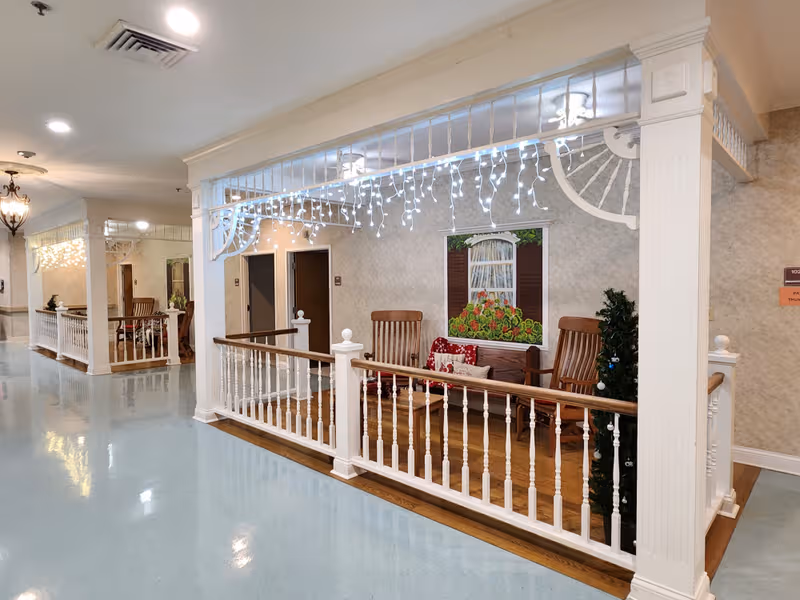 Interior hallway of The Heritage Nursing and Rehabilitation Facility with a lounging area and decorative railing.