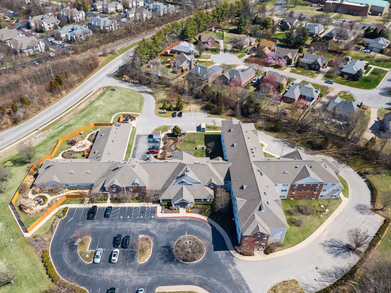 Aerial view of a senior living facility complex with parking lot, landscaped grounds and surrounding residential neighborhood.