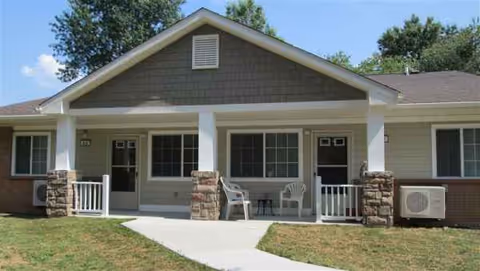Front view of a single-story senior living facility with a covered porch and chairs.