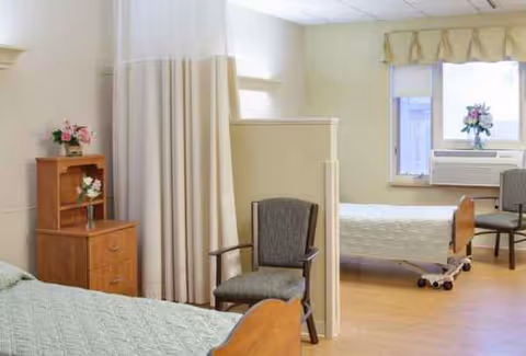 Shared senior living bedroom with two beds, a divider, chairs, and a window.