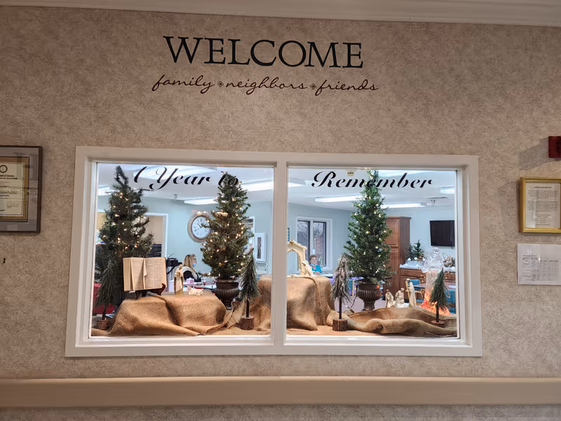 A warmly decorated lobby seen through a large window with Christmas trees and a 'Welcome' sign.