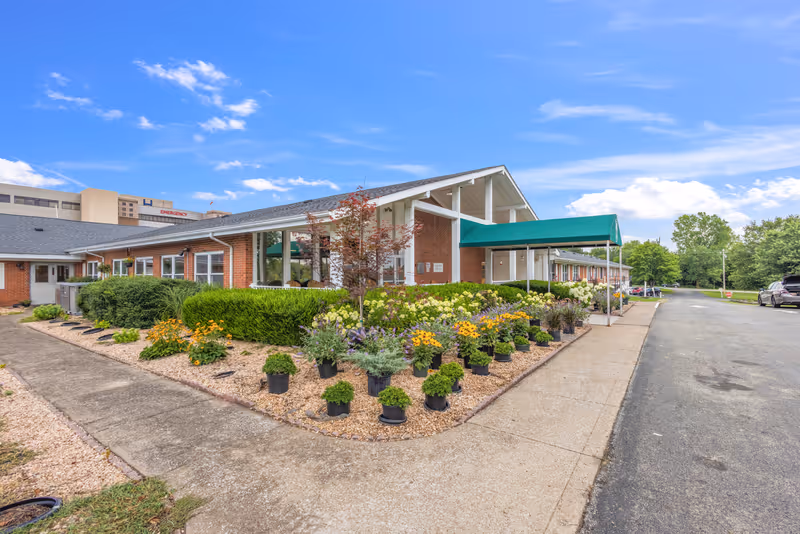 Senior living facility exterior with brick facade, landscaped entrance, and potted flowers.