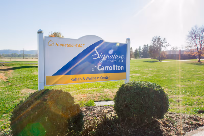 Outdoor freestanding sign for Signature HealthCARE of Carrollton Rehab & Wellness Center on a grassy lawn with shrubs and trees.