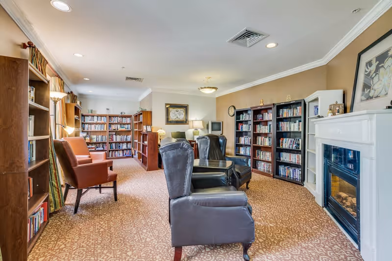 Cozy reading room with bookshelves, upholstered and leather chairs, and a fireplace.