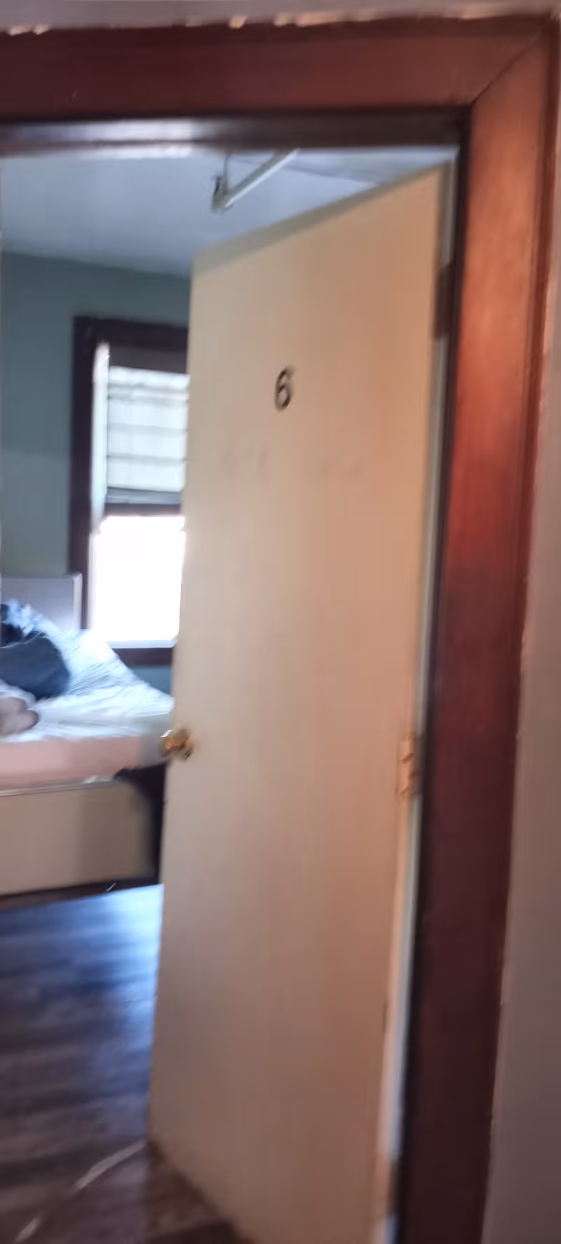 Open door to a bedroom with a bed and window in a senior facility.