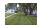 Exterior view of a senior living facility with green lawn, trees, and a walkway.