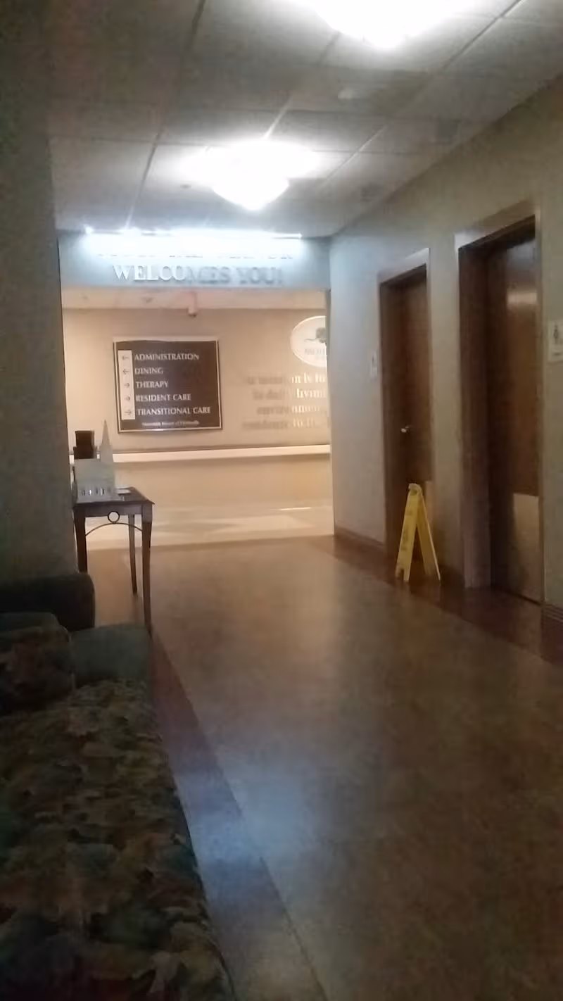 Dim hallway inside Mountain Manor of Paintsville with signs, doors, and a caution sign.