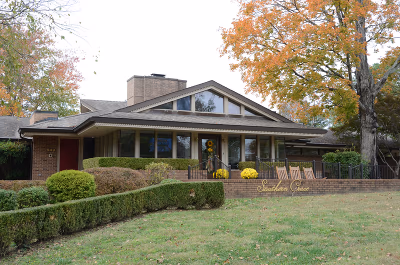 Single-story brick assisted living facility with large windows, front entrance, and outdoor seating.