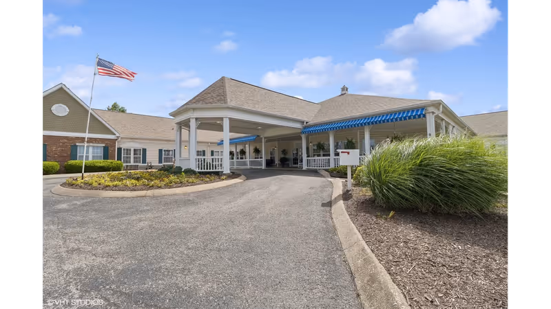 Front entrance of The Neighborhood at Hopkinsville with a covered porte-cochere, American flag, and landscaped driveway.