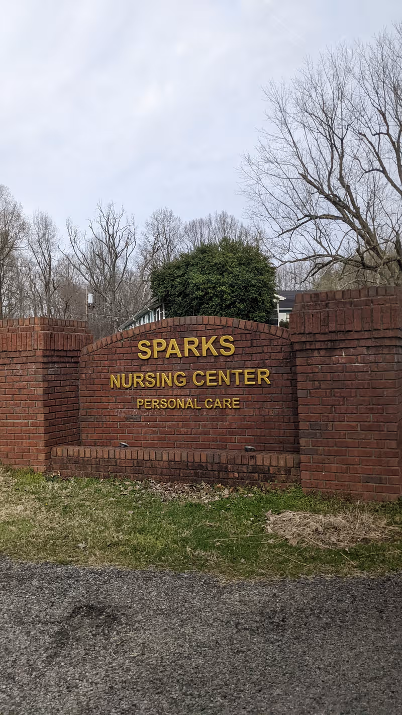 Brick entry sign reads Sparks Nursing Center Personal Care with trees in background.