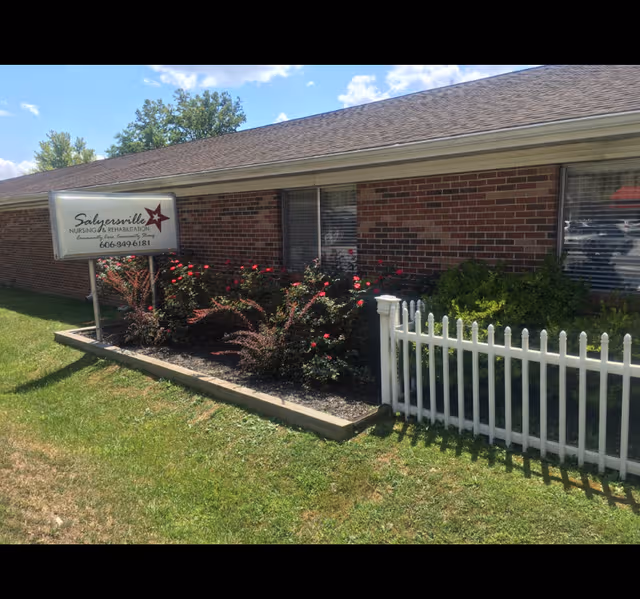 Brick facility front with Salyersville Nursing & Rehab sign and white picket fence.