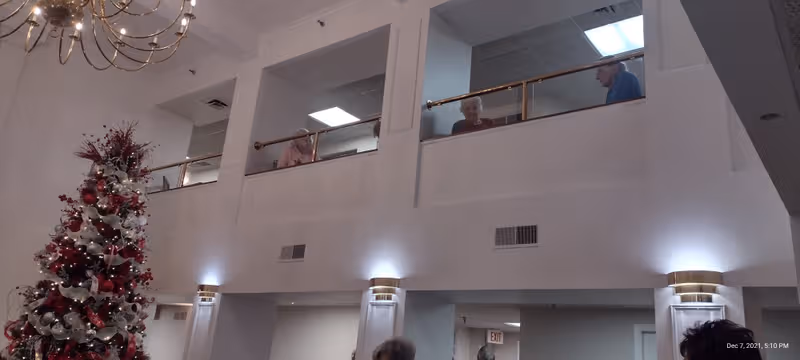 Interior atrium of a senior living facility featuring a Christmas tree and residents on a balcony.