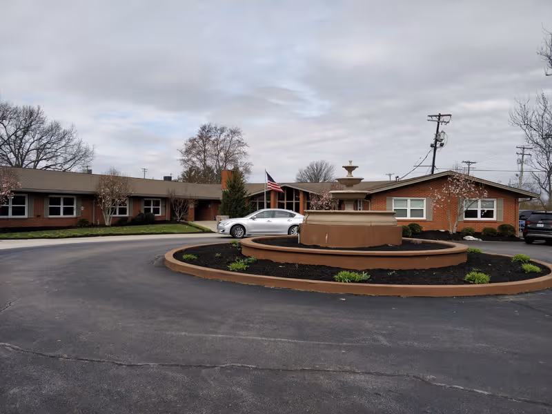 Brick senior living facility with circular driveway and central fountain.