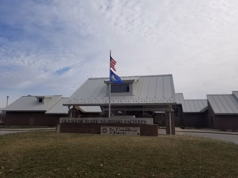 Front exterior of Glasgow State Nursing Facility with flagpole, sign, and brick building.