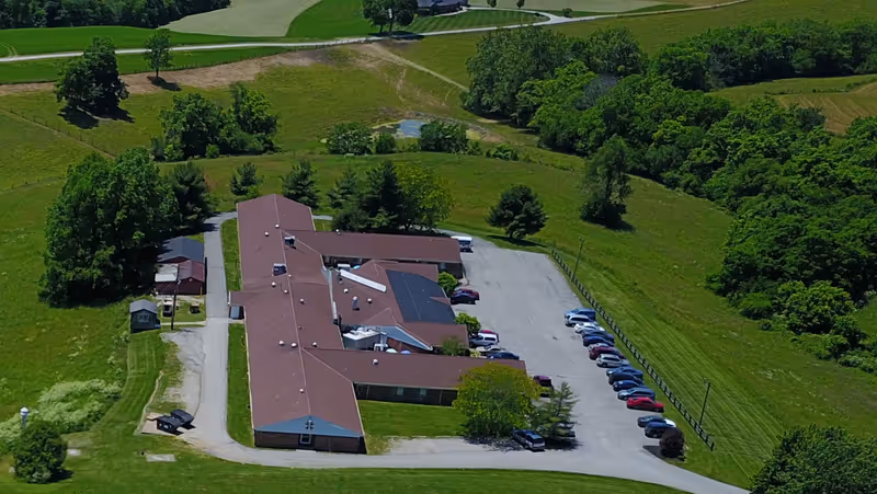 Aerial view of a brown-roofed senior living facility with a large parking lot and green surroundings.