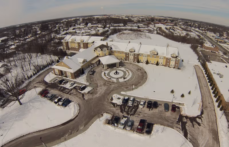 An aerial view of a snow-covered senior living campus with a circular driveway and parking.