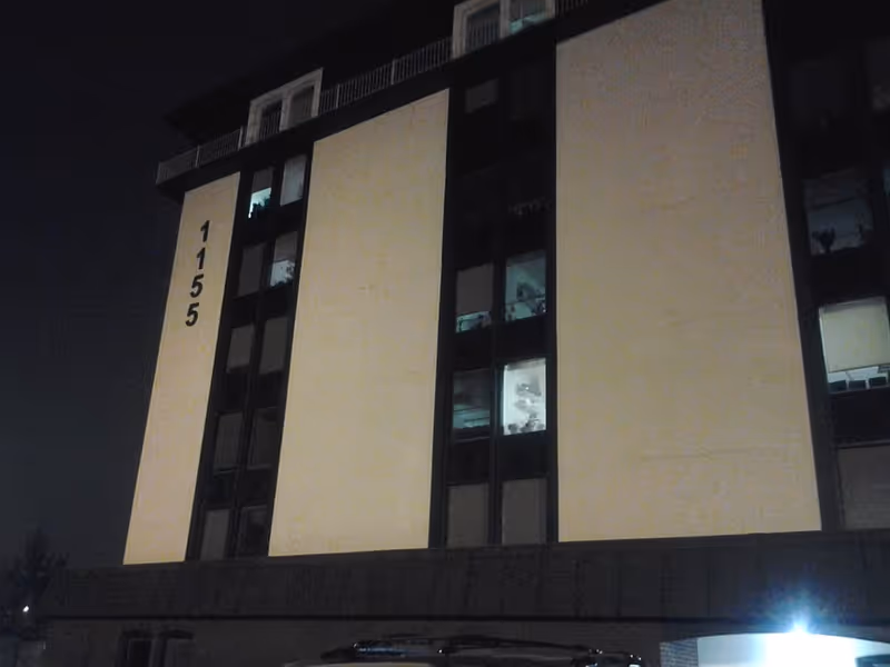 Nighttime exterior of a multi-story building with vertical address numbers 1155.
