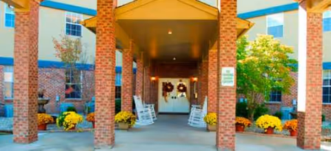 Covered brick entrance at Brookdale Murray with rocking chairs and yellow mums.