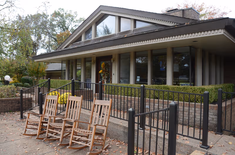 Front view of a senior living facility with a covered entrance and outdoor seating.