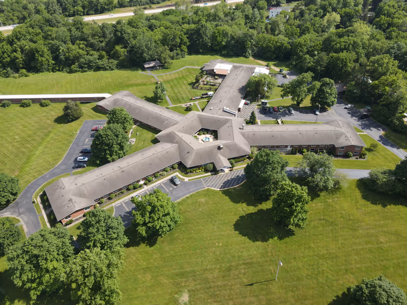 Aerial view of a star-shaped senior living facility with multiple wings around a central courtyard, surrounded by lawns, parking lots, and trees.