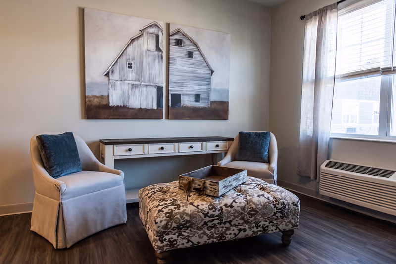 Cozy living room seating with two chairs, ottoman, console, and barn artwork.